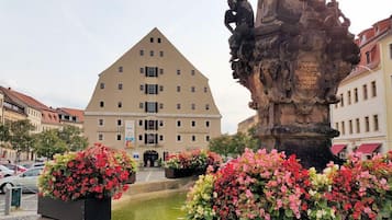 A building with a triangular roof and multiple windows, surrounded by flower beds and a fountain.