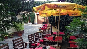 An outdoor patio with wooden tables and chairs, red cushions, and a yellow umbrella with the brand name 'Sujany'. - Schwarzer Bär (Zittau)