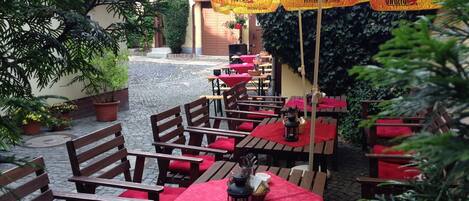 An outdoor patio with wooden tables and chairs, red cushions, and a yellow umbrella with the brand name 'Sujany'.