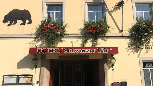 A hotel facade with a bear logo, red signage, and flower boxes. - Schwarzer Bär (Zittau)