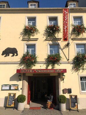 A hotel facade with a bear logo, red signage, and flower boxes. - Schwarzer Bär (Zittau)
