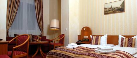 A hotel room with a bed, a desk, a chair, a table, and a lamp.