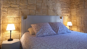 Ein Schlafzimmer mit Steinwand, einem weißen Bett mit floralem Bettzeug und zwei Nachttischlampen.