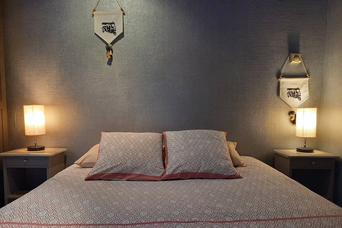 Un lit bien fait, avec une literie à motifs, deux lampes de chevet et un élément décoratif fixé au mur.
