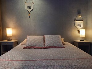 Un lit bien fait, avec une literie à motifs, deux lampes de chevet et un élément décoratif fixé au mur.