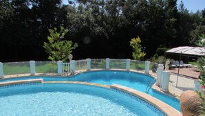 Ein Schwimmbecken mit klarem, blauem Wasser, umgeben von einem weißen Zaun und einer gepflasterten Liegefläche.