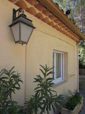 Un bâtiment à la façade beige, une fenêtre avec des volets blancs et une lanterne fixée au mur.