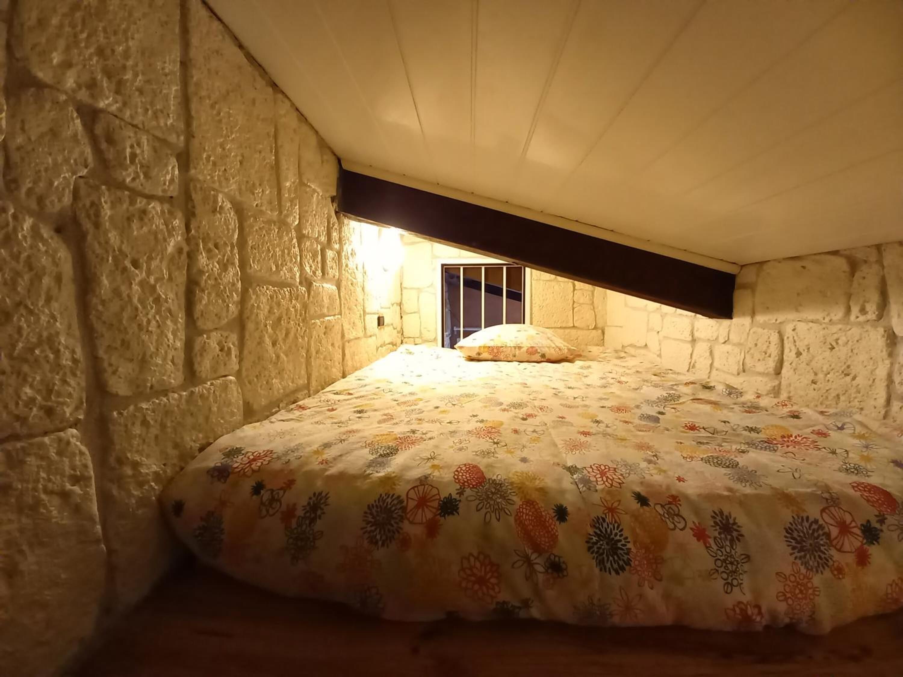 Quarto com parede de pedra, teto de madeira e cama com colcha estampada.