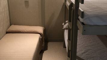 Una habitación pequeña, con poca luz, que tiene dos literas, una cama individual y una lámpara fijada a la pared.