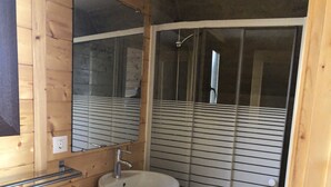Een badkamer met een houten wastafelmeubel, een wastafel, een spiegel en een douche met horizontale luiken.