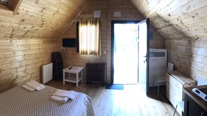 Een knus houten kamer met een bed, een tafeltje, een stoel, een bureau en een radiator.