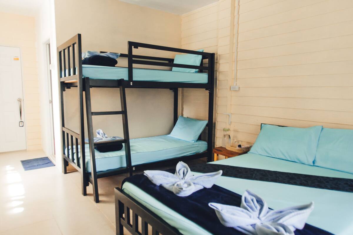 Een slaapkamer met stapelbed, bureau en stoel, een witte deur en een plafondventilator.
