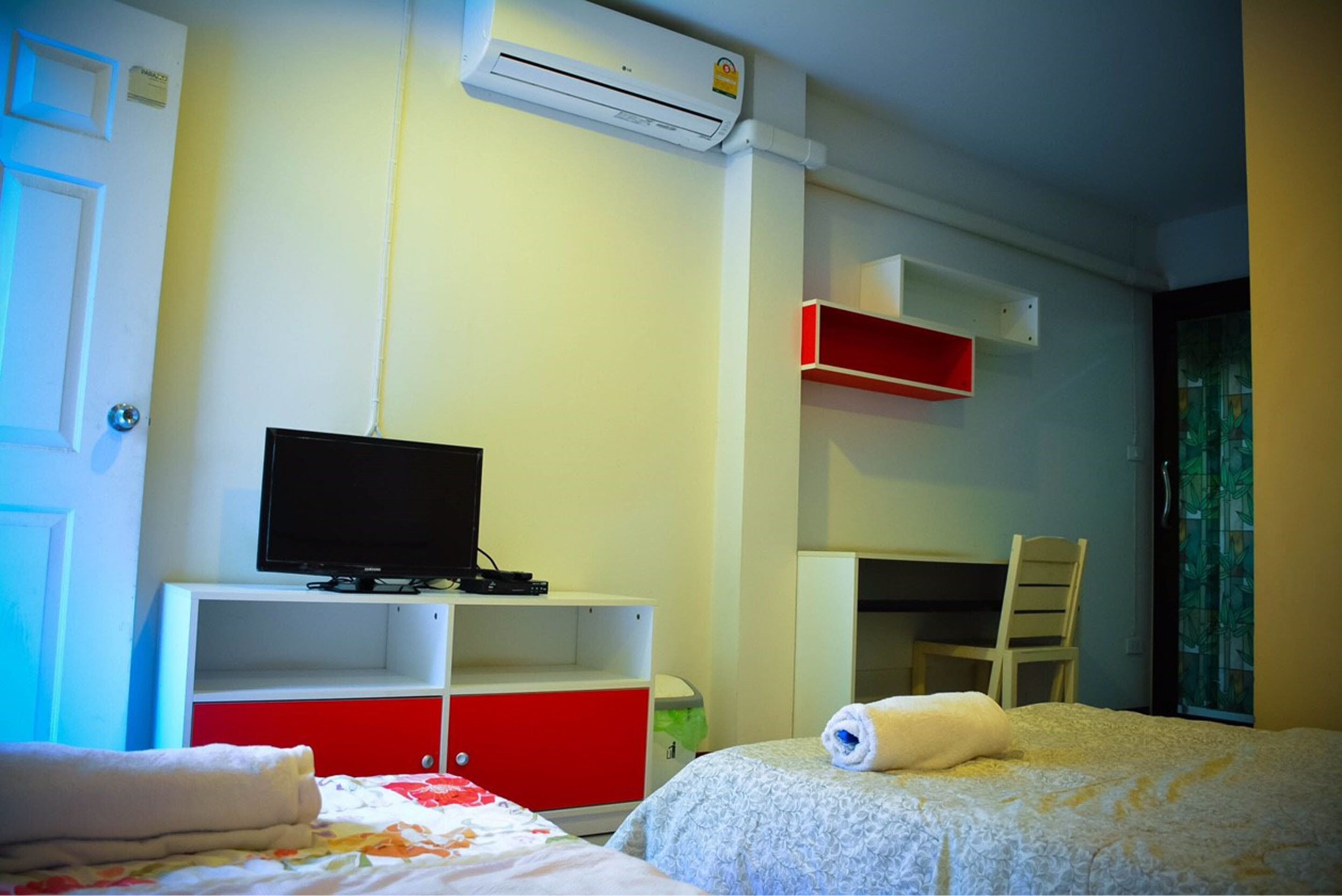 A hotel room with a bed, a desk, a chair, a television, and an air conditioning unit.