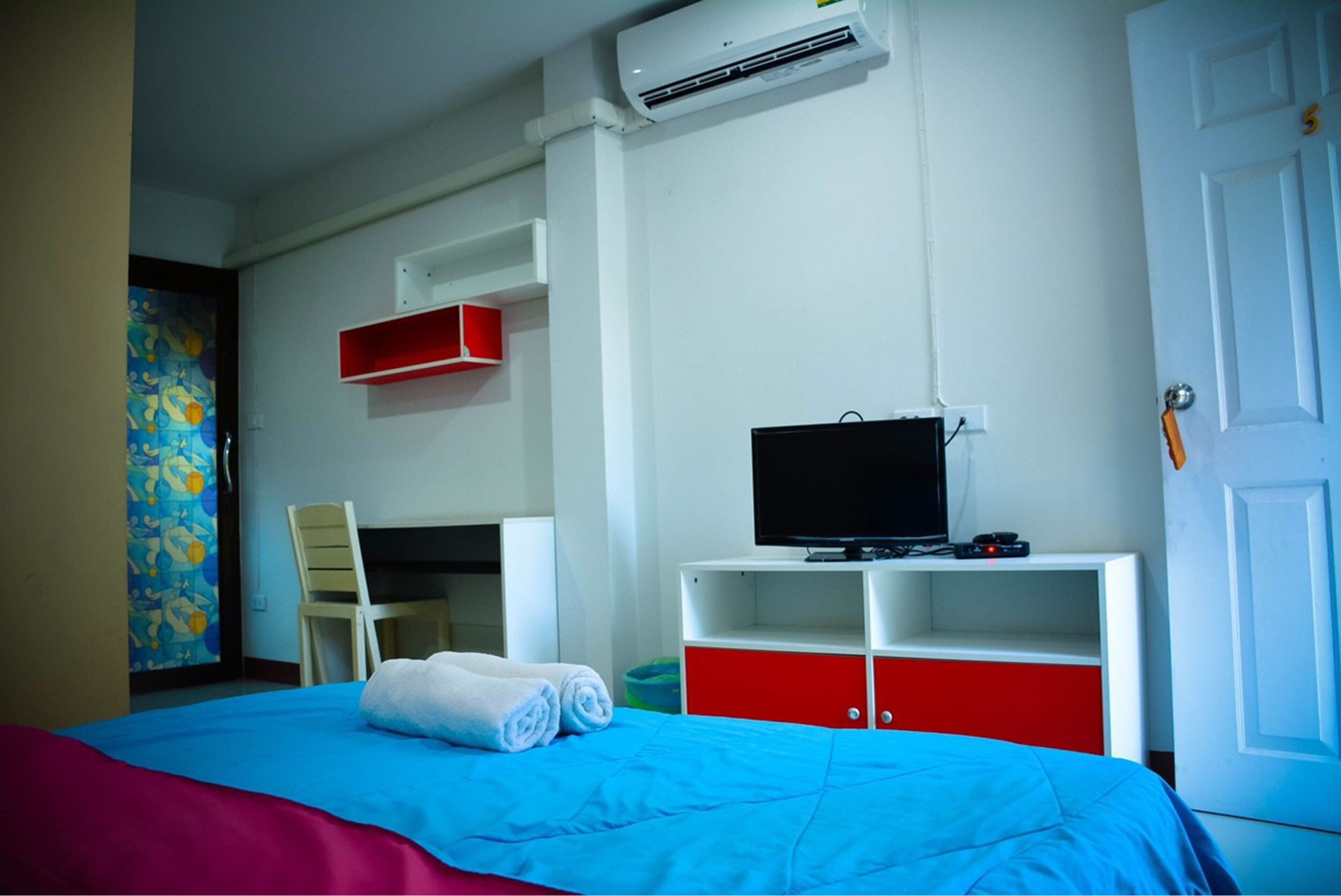 A hotel room with a bed, a desk, a TV, and a red storage unit.