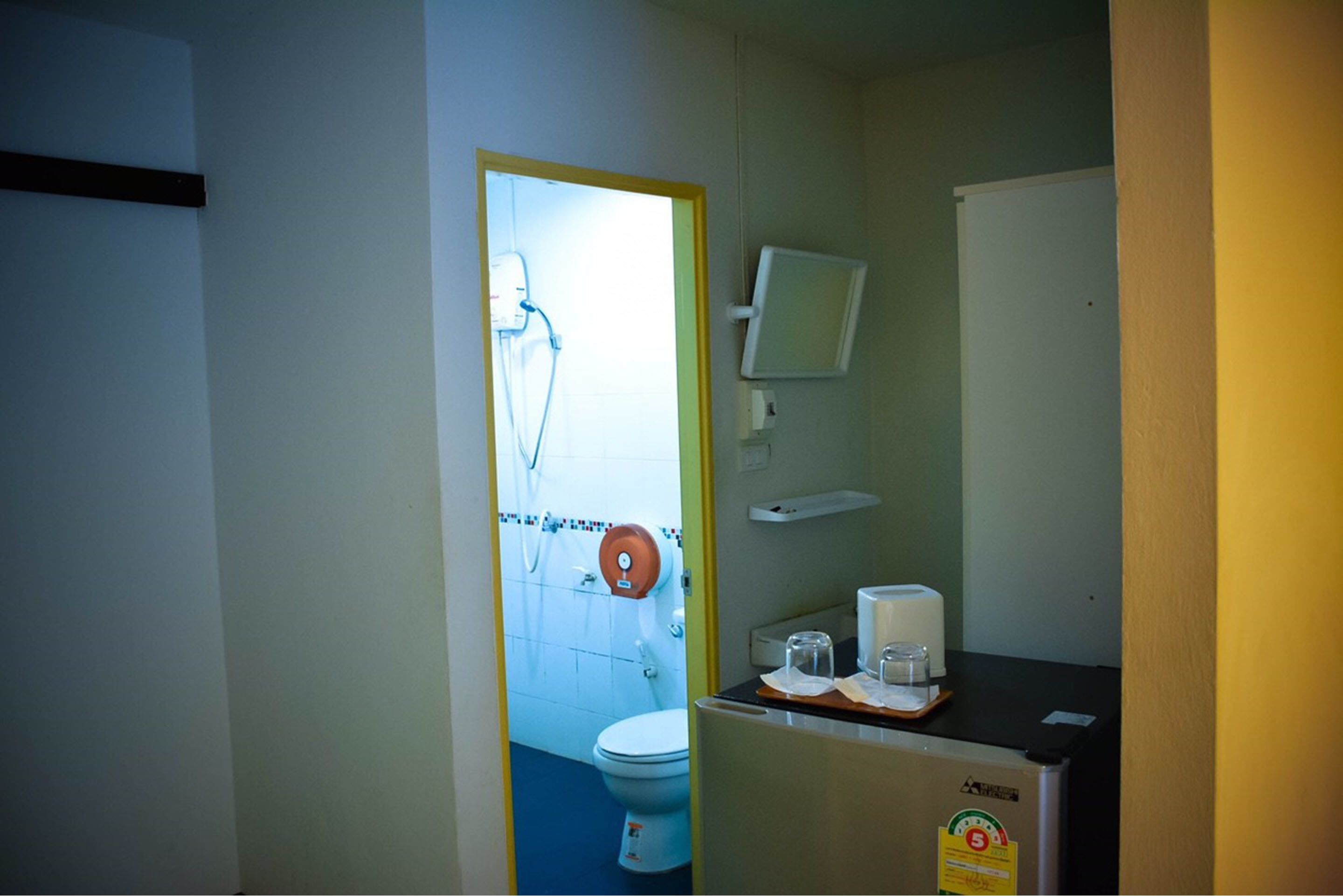 Baño pequeño con inodoro, ducha y lavamanos. Hay un espejo sobre el lavamanos y un dispensador de toallas en la pared.