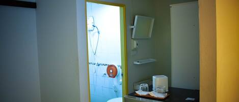 Baño pequeño con inodoro, ducha y lavamanos. Hay un espejo sobre el lavamanos y un dispensador de toallas en la pared.