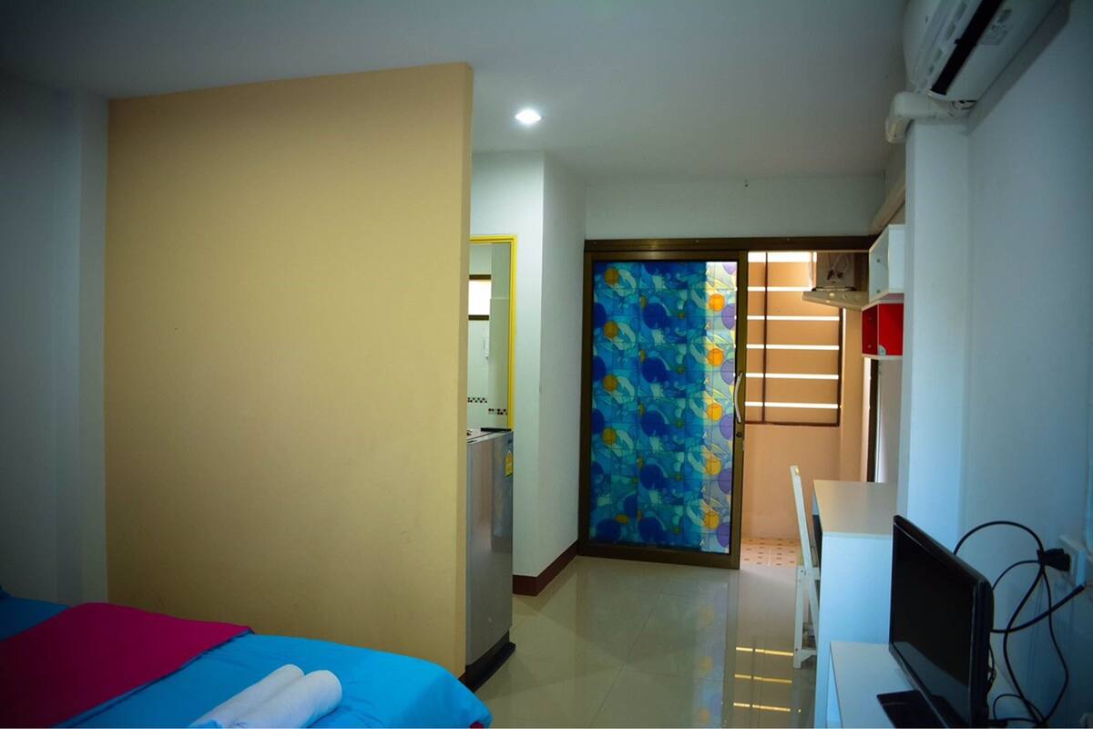 A hotel room with a bed, a desk, a chair, a TV, and a bathroom visible through a door.