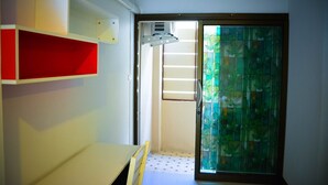 A room with a sliding glass door leading to a balcony, a white desk, and a red shelf unit. - Sabaidee Place (Phetchabun)