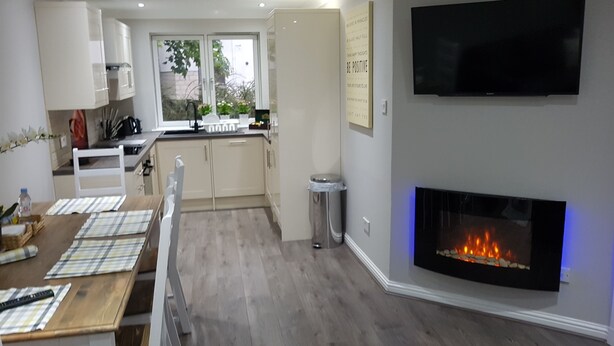 A modern living room with a fireplace, a flat-screen TV, and a dining area with a table and chairs. - First St John's Hill Apartment 2 (Edinburgh)