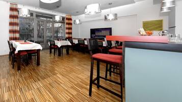 A dining area with wooden flooring, tables with white tablecloths, and red chairs.