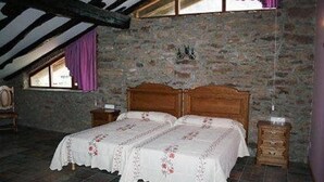 Une chambre à coucher avec un lit en bois, des murs en pierre et une fenêtre ornée de rideaux violets.
