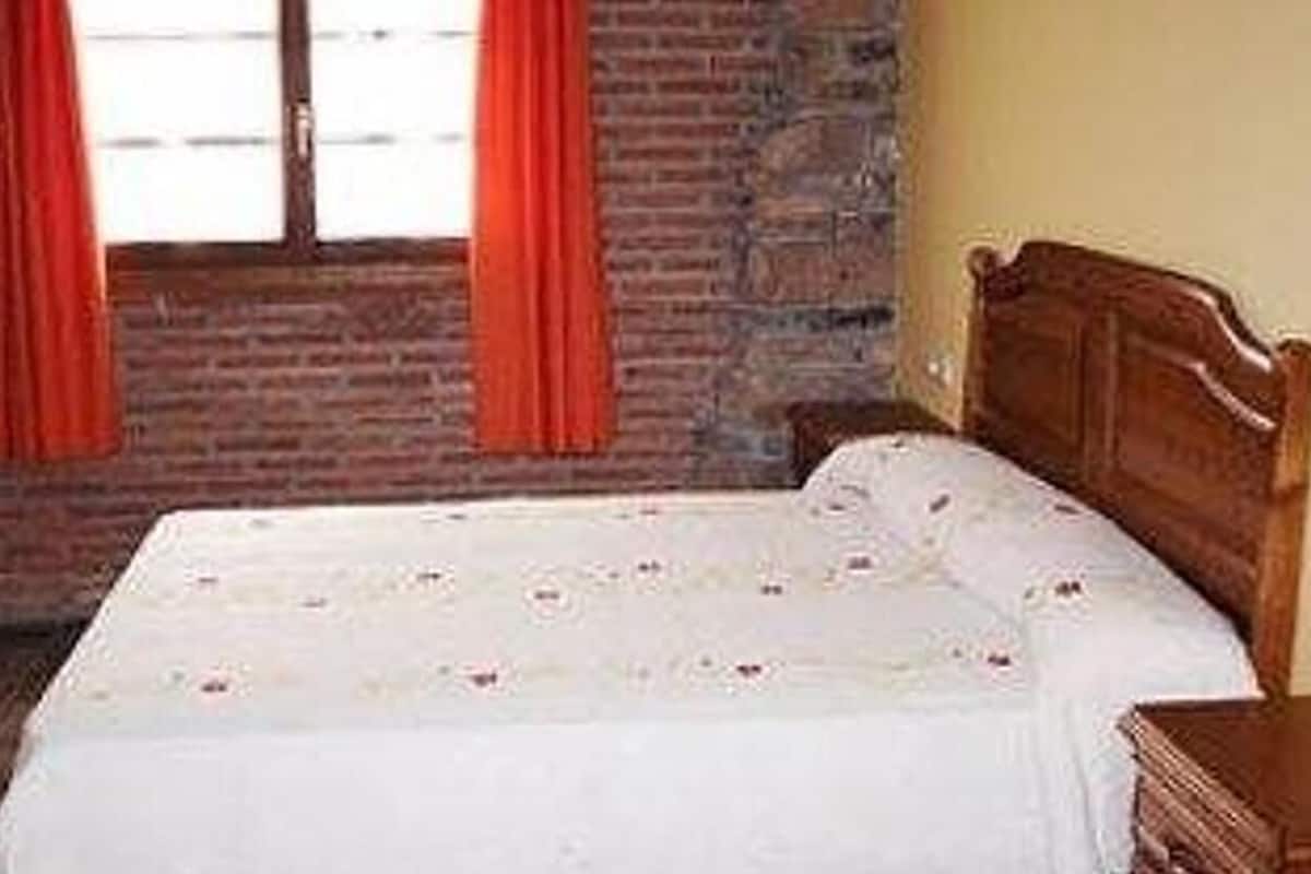 Une chambre avec un lit en bois, un mur en briques et une fenêtre ornée de rideaux rouges.