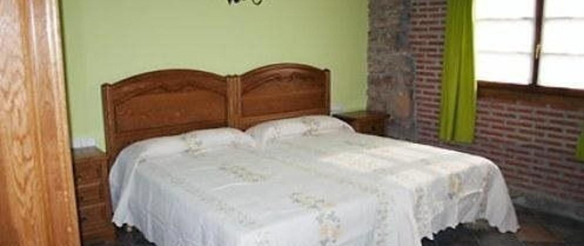 Un letto singolo con una testiera in legno, in una stanza con parete in mattoni e finestra.