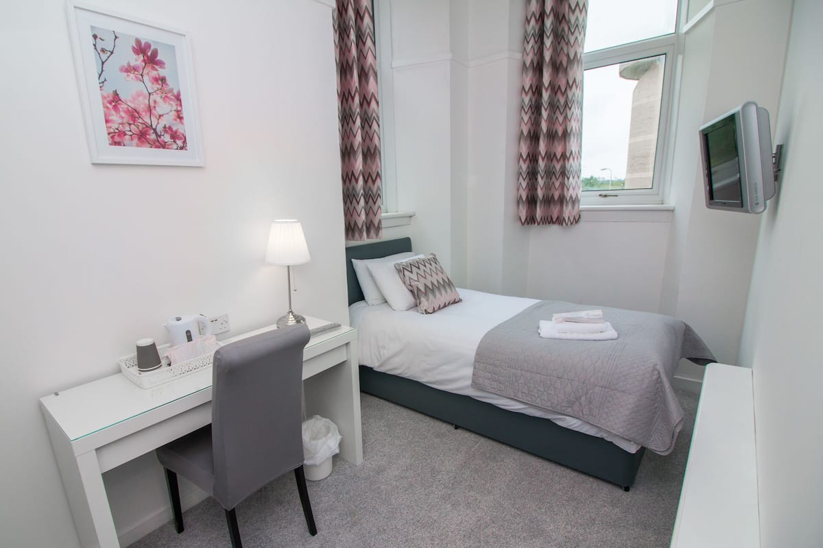 A bedroom with a bed, a desk, a chair, a lamp, and a TV.