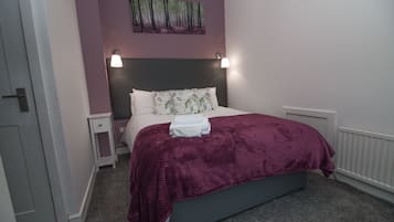 A bedroom with a bed, a nightstand, a wall-mounted lamp, and a radiator.