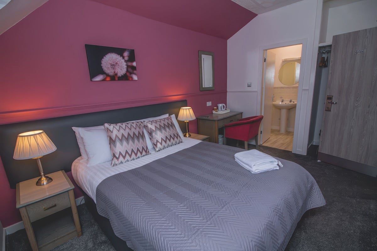 A bedroom with a bed, bedside tables, a desk, and a bathroom visible through an open door.