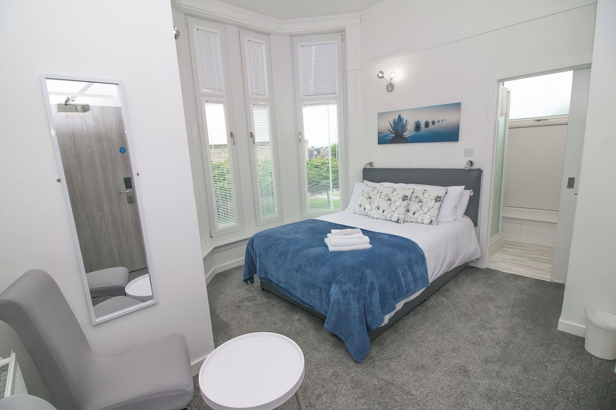 A bedroom with a bed, a chair, a small table, and a window with blinds.