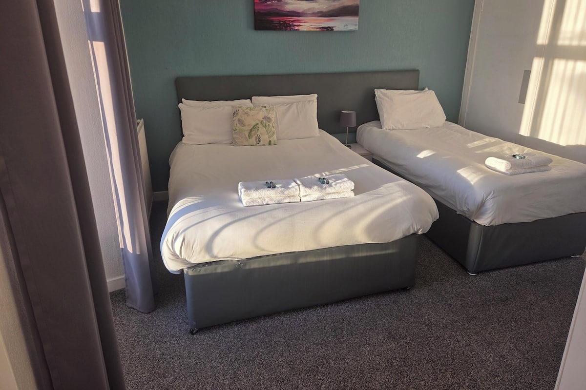 A hotel room with two beds, a painting on the wall, and a window with curtains.