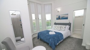 A bedroom with a bed, a chair, a small table, and a window with blinds. - Bentley Hotel (Motherwell)