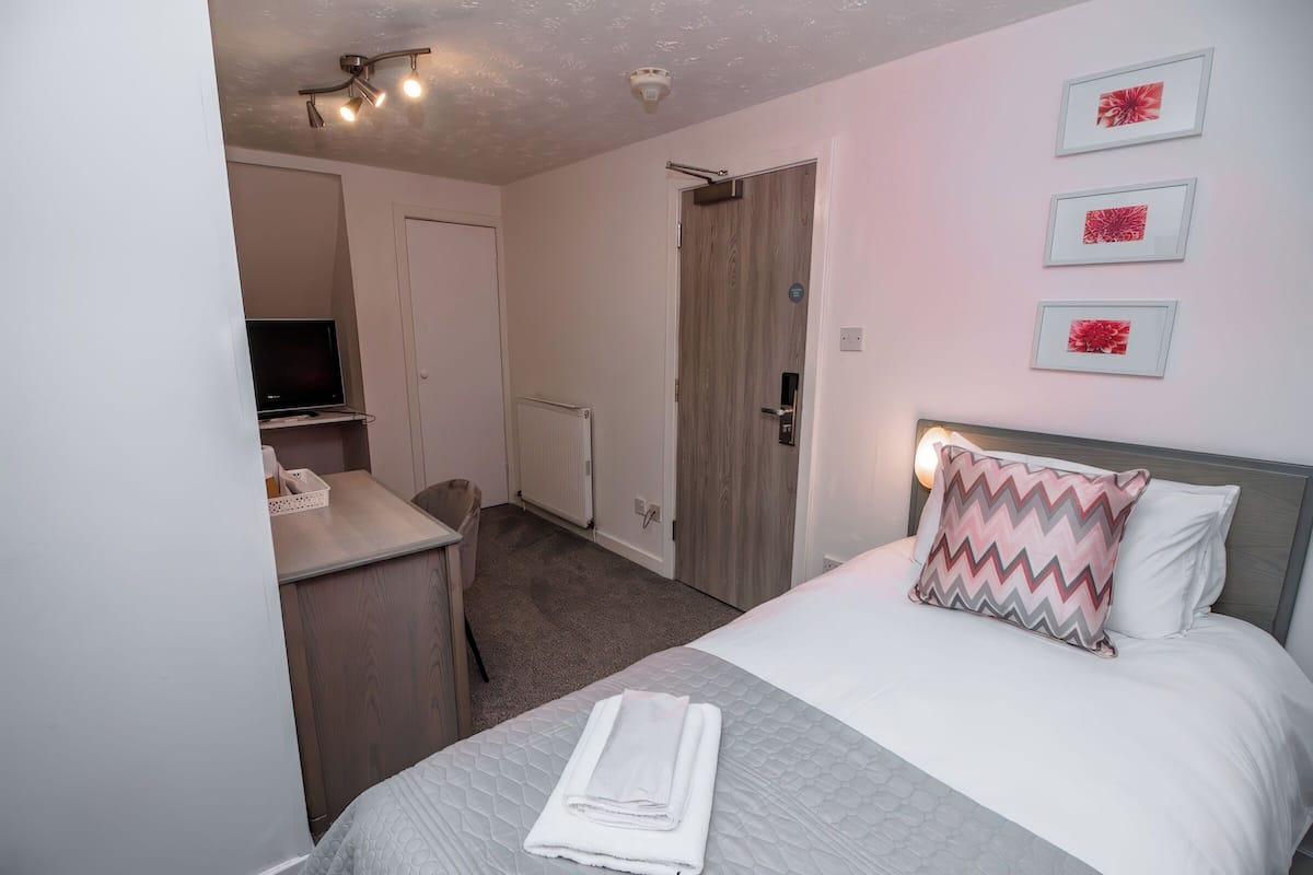 A bedroom with a bed, a desk, a television, and a door.