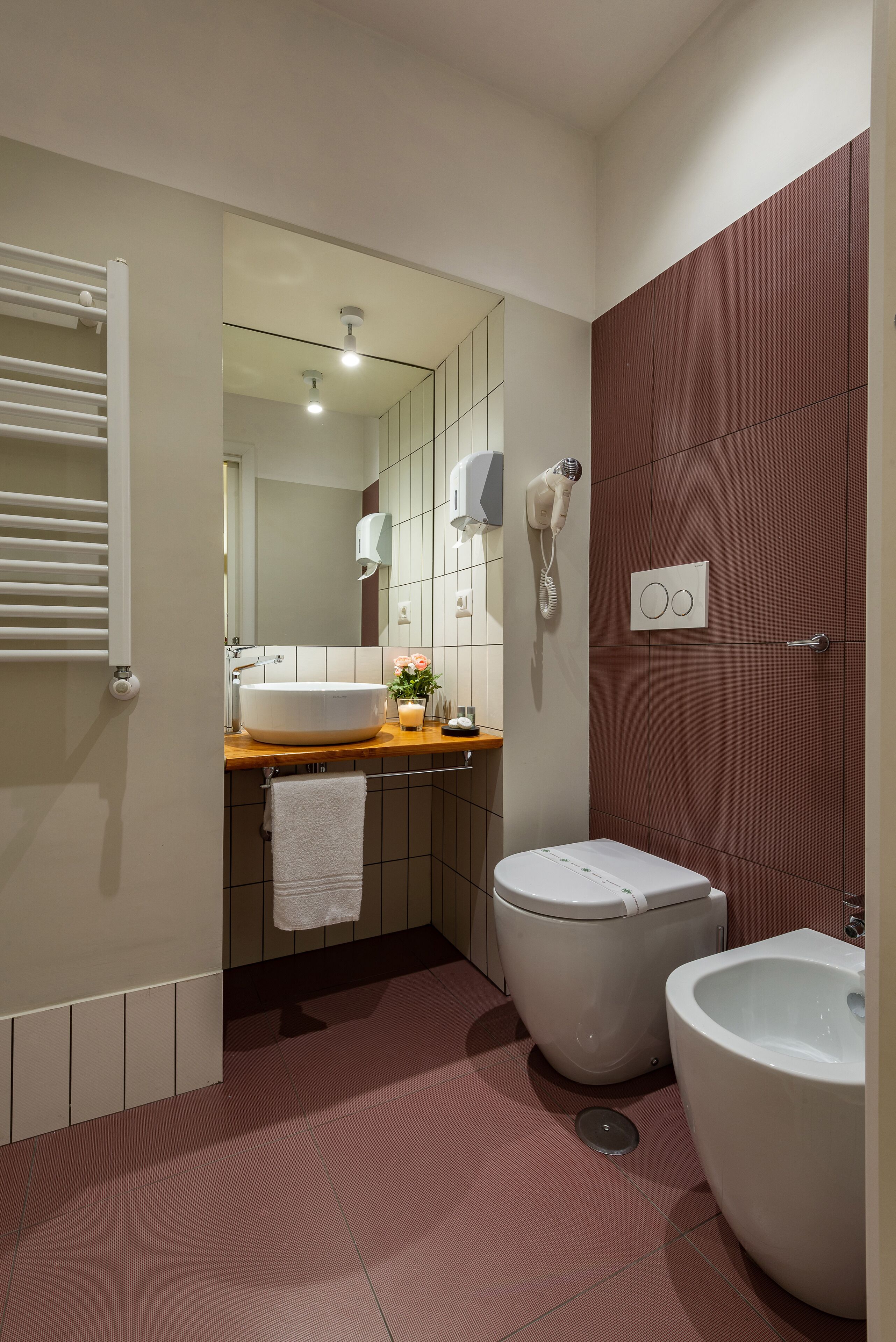 A modern bathroom with a large sink, two toilets, a bidet, a towel rack, and a hairdryer.