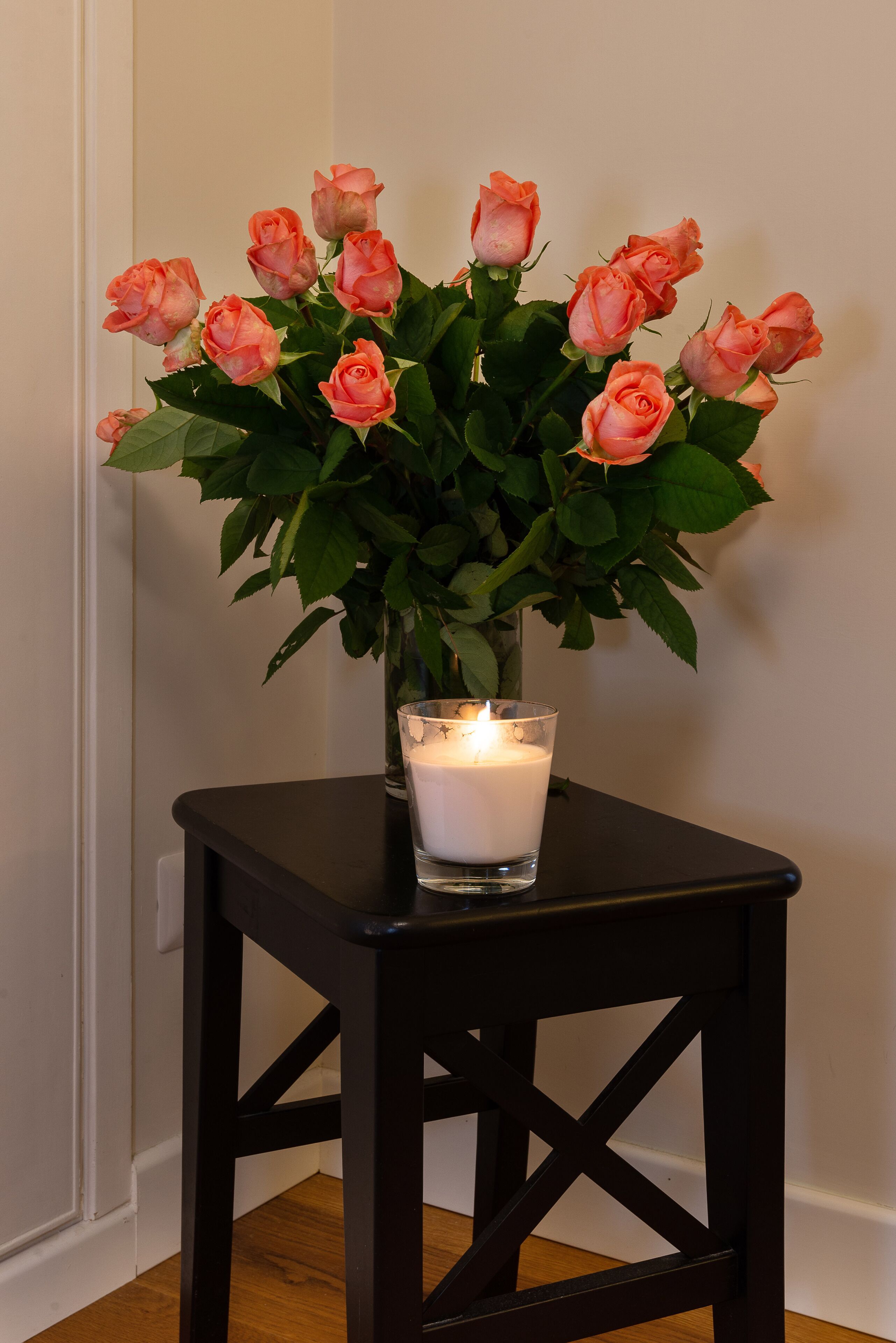 A black table with a vase of pink roses and a lit candle.