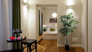 A modern hotel room with a wooden floor, a small dining table with wine glasses, a potted plant, and a bed with a headboard. - Tula Inn (Rome)