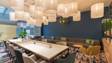 Een moderne vergaderruimte met een lange tafel, meerdere stoelen, een bank en hangende吊灯.