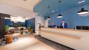 A modern hotel reception area with a blue accent wall, a reception desk, and a seating area with chairs and tables. - Hampton by Hilton Utrecht Central Station (Utrecht)