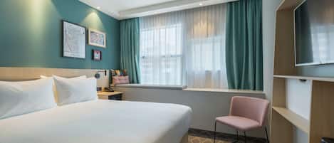 Habitación de hotel con una cama grande, una silla, televisión, ventana con cortinas y obras de arte en la pared.