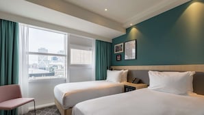 A hotel room with two beds, a chair, a nightstand, and a window with curtains. - Hampton by Hilton Utrecht Central Station (Utrecht)