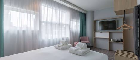 Una habitación de hotel con una cama grande, un televisor en un estante de madera, una silla y un armario.