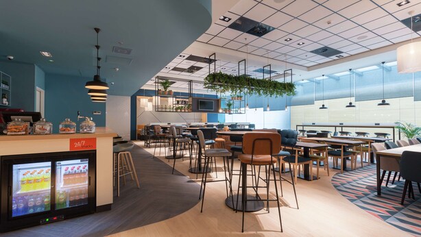 A modern restaurant with a counter, seating area, and a large window. - Hampton by Hilton Utrecht Central Station (Utrecht)
