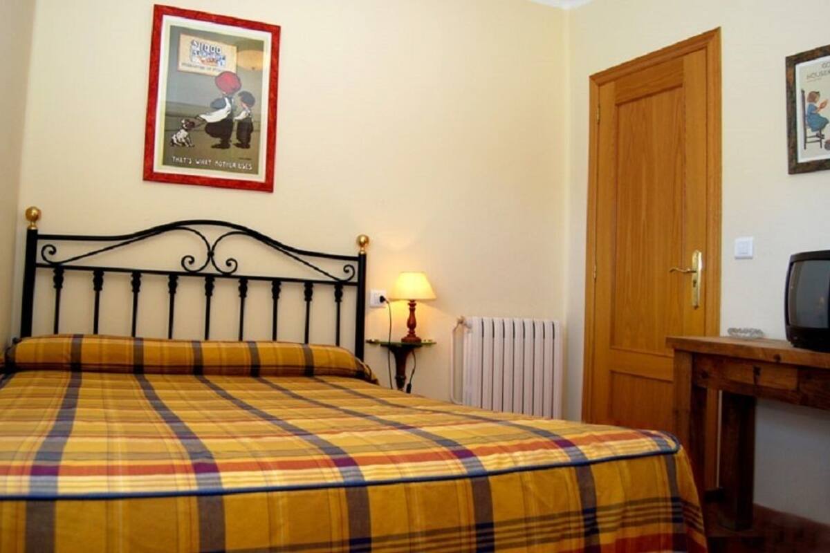 A bed with a plaid bedspread, a bedside lamp, a framed picture on the wall, and a wooden door.