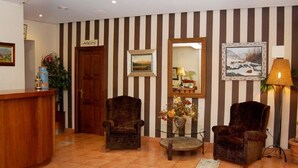 A reception area with striped wallpaper, two armchairs, a wooden reception desk, a mirror, a vase with flowers, and a lamp. - Valle de San Emiliano (San Emiliano)