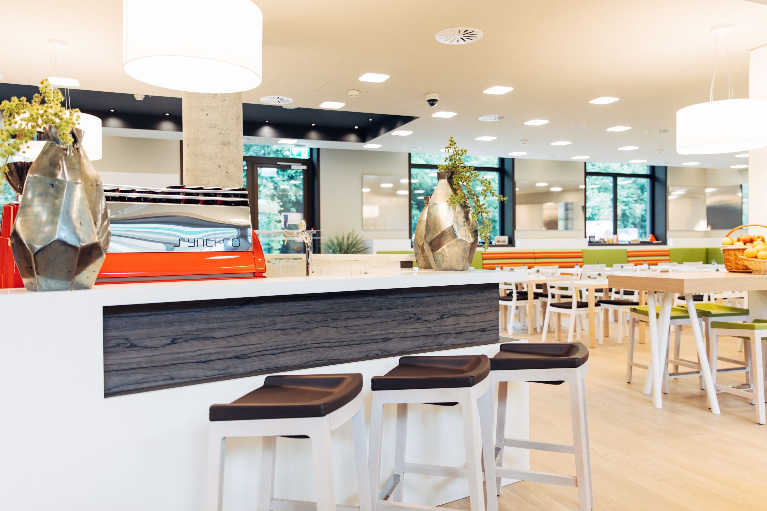 A modern restaurant with a white bar area, multiple seating options, and large windows providing views of the outdoors.