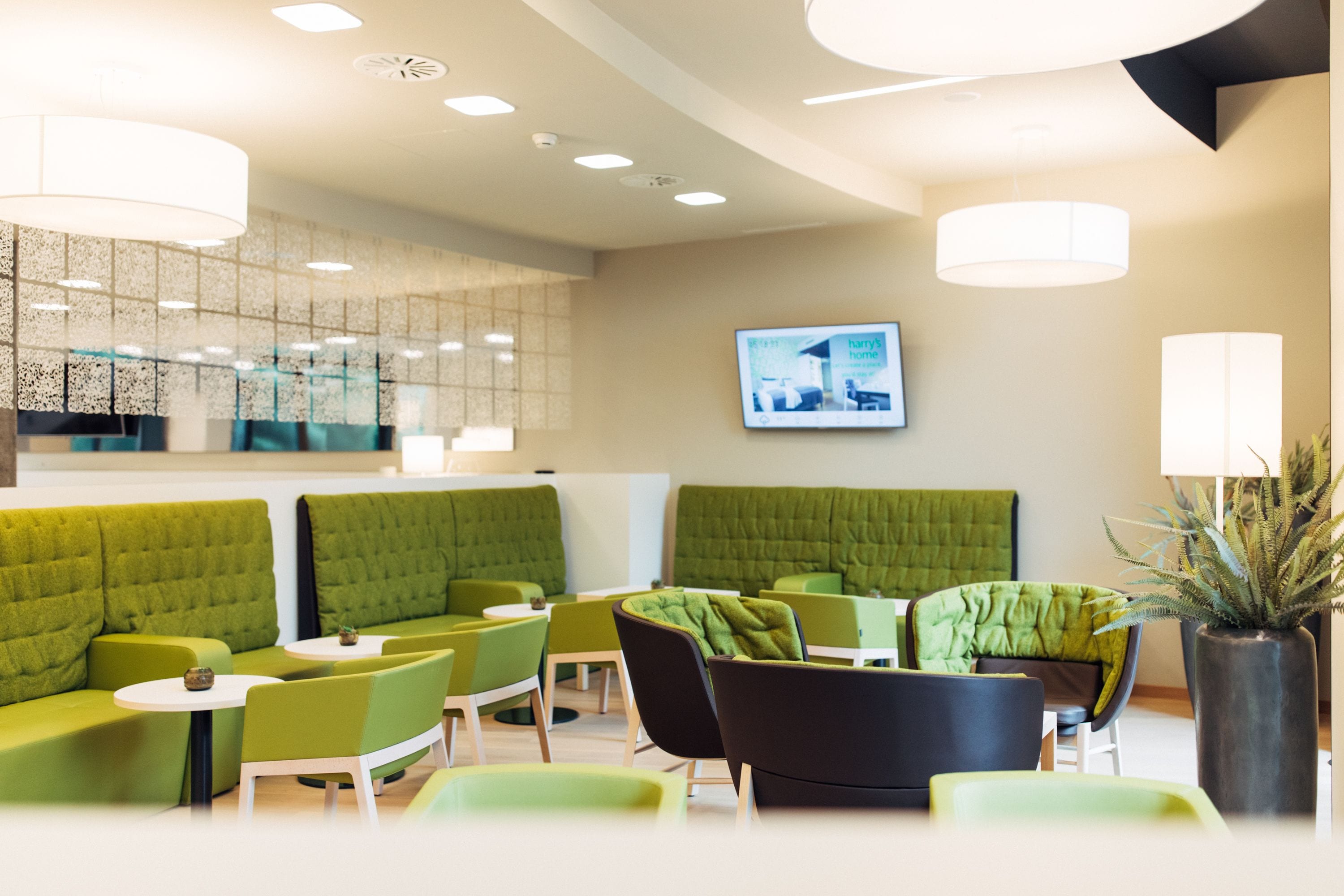 Ein moderner Lounge-Bereich mit grünen Polstersesseln, weißen Tischen und Pendelleuchten.