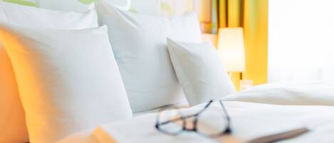 A bed with white pillows and a book with glasses on it.