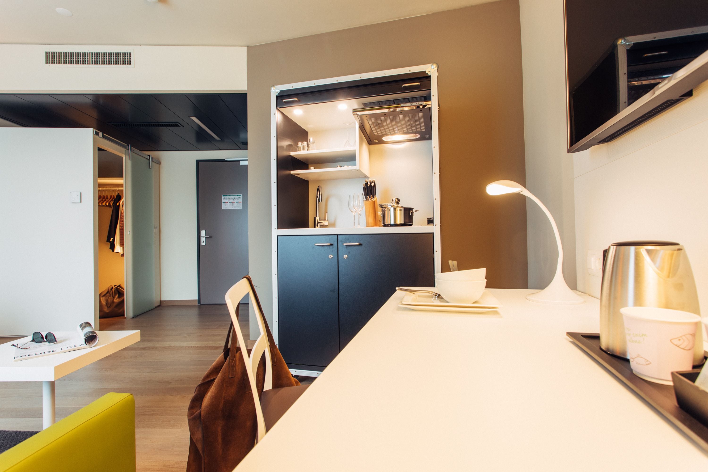 A modern kitchen with a built-in oven, a coffee machine, and a microwave. There is a dining table with chairs and a lamp.