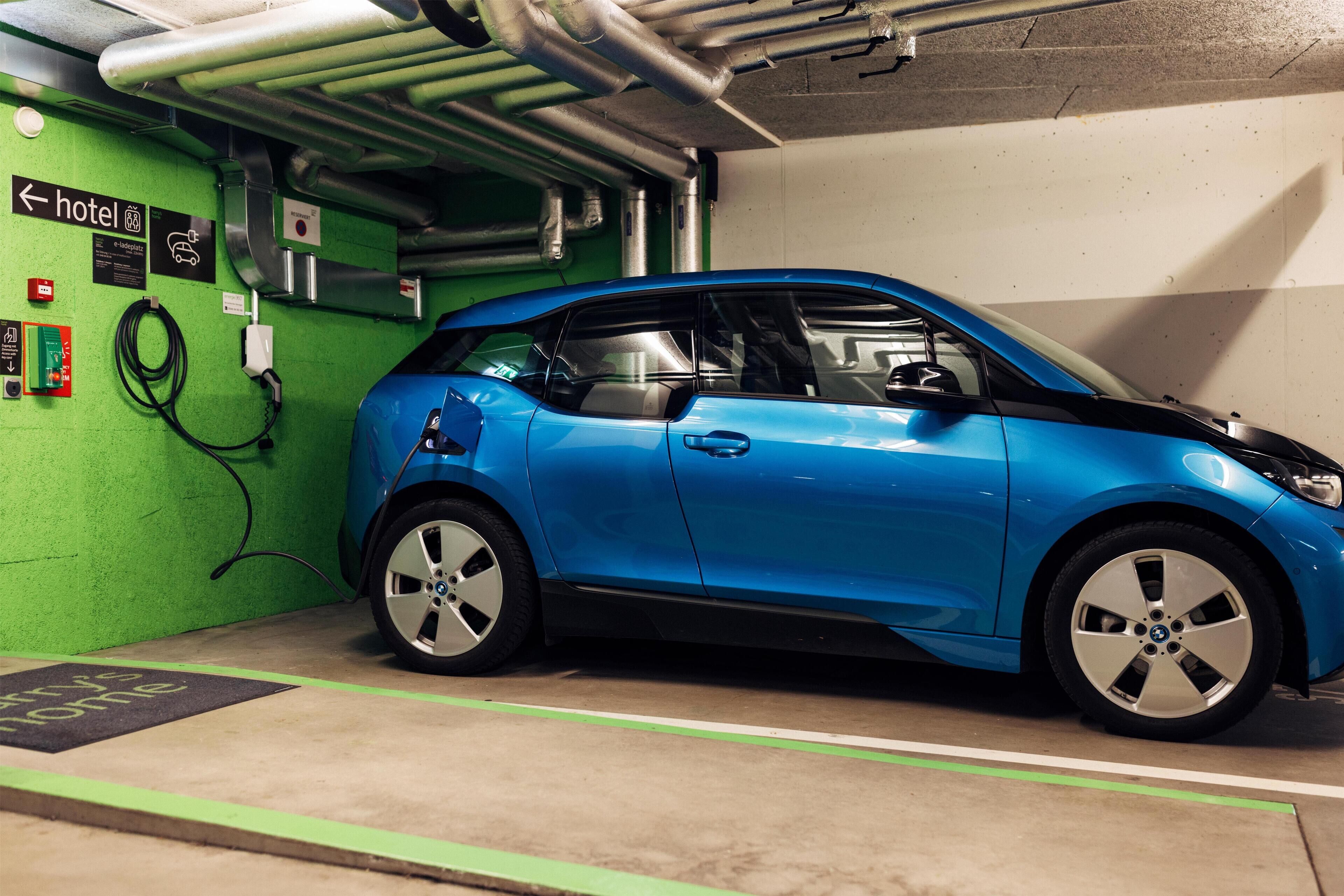 Ein blaues Auto steht in einer grün-weißen Parkgarage, ein Schild weist auf ein Hotel in der Nähe hin.